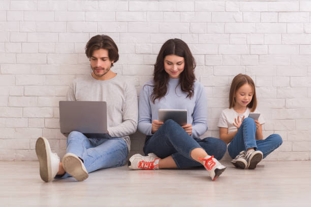 happy family of three sitting on floor with different gadgets - laptop women child digital tablet imagens e fotografias de stock