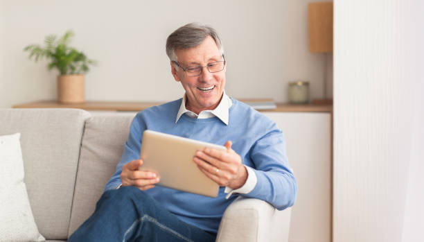 istock Cheerful Senior Man With Digital Tablet Sitting On Couch Indoor 1202955149