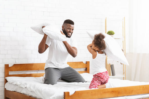 istock Laughing black man having pillow fight with little daughter 1202956160