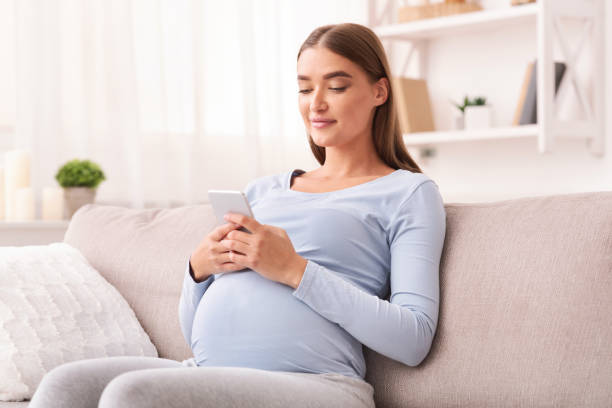 istock Expectant Girl Using Smartphone Texting Sitting On Sofa At Home 1202956485