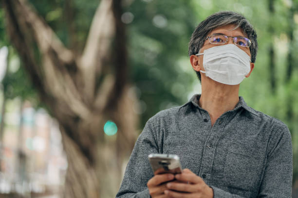 istock Man with surgical mask protecting himself from corona virus using mobile on the street 1202956660