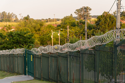 view of a green metal fence in a residential condominium and over it the barbed wire retaining rollers extended to guarantee safety. Residential condominiums in Brazil.