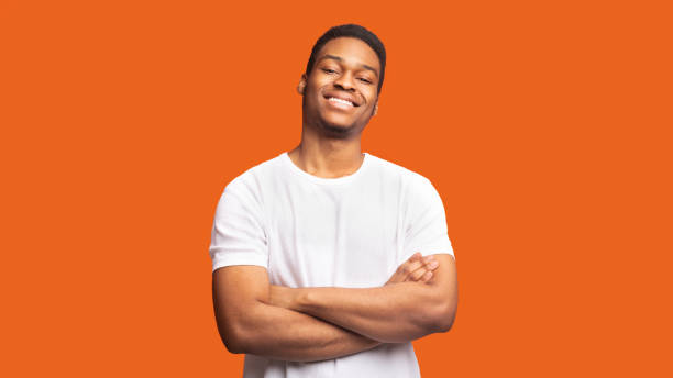 Smiling afro guy portrait on orange background Confident Guy. Happy black man looking at camera with crossed arms folded, panorama, copyspace, orange wall men hairstyle afro cool stock pictures, royalty-free photos & images