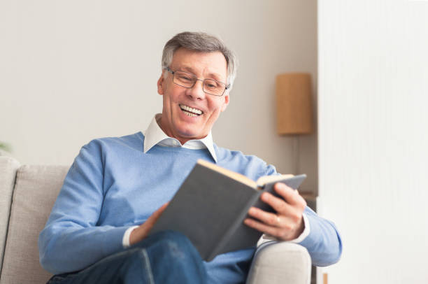 istock Senior Man Reading Book Sitting On Sofa At Home 1202957748