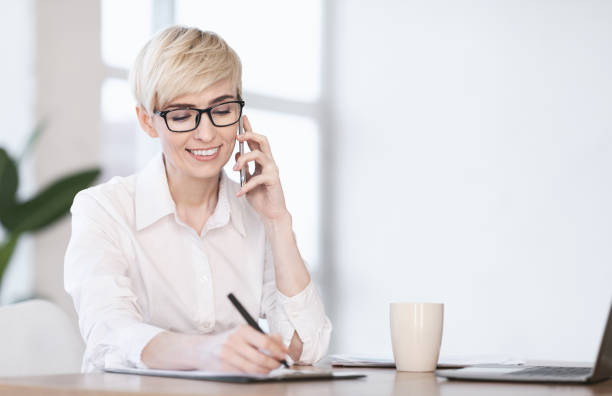 istock Entrepreneur Lady Talking On Phone Taking Notes Sitting At Workplace 1202959001