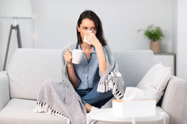istock Sick woman wrapped in blanket drinking hot coffee 1202960514