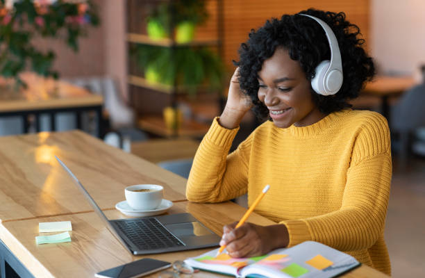 Smiling african girl in headphones looking at laptop, cafe interior Smiling african american girl in wireless headphones looking at laptop, studying foreign language through video conference application, cafe interior, copy space bushy stock pictures, royalty-free photos & images