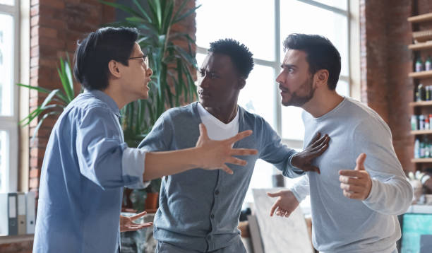 Multiracial coworkers having quarrel in office, conflict of interest Office conflict. Angry multiracial young men fighting at workplace, afro guy standing between them spar stock pictures, royalty-free photos & images