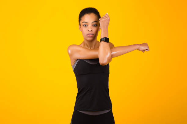 woman exercising stretching deltoid arm muscle posing over yellow background - body building determination deltoid wellbeing imagens e fotografias de stock