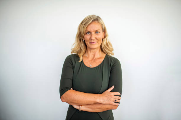 Portrait of Confident Mature Businesswoman Front view close-up of mature Caucasian businesswoman in early 50s standing with arms crossed and smiling at camera. medium length hair stock pictures, royalty-free photos & images