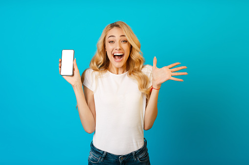 Great offer. Surprised girl showing phone with blank screen, blue background