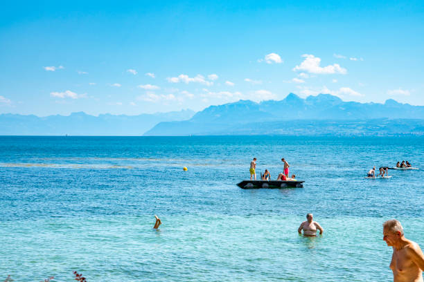Lake Geneva, Switzerland.  This is one of the many swimming areas around the lake with jetties and floating platforms with tourists in front of the Alps mountain range across Lake Geneva.