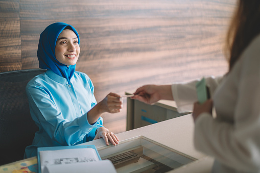 malaysia hospital registration counter asian female receptionist getting payment from the female hijab Muslim patient accepting her credit card
