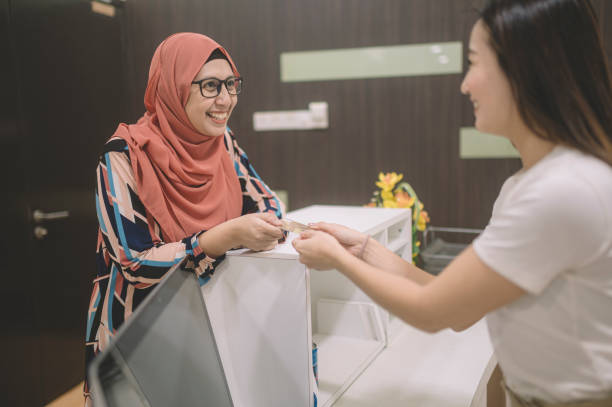 uma paciente asiática pagando sua conta hospitalar no balcão de registro com seu cartão de crédito entregue para o caixa feminino - dentist office built structure doctors office retail - fotografias e filmes do acervo