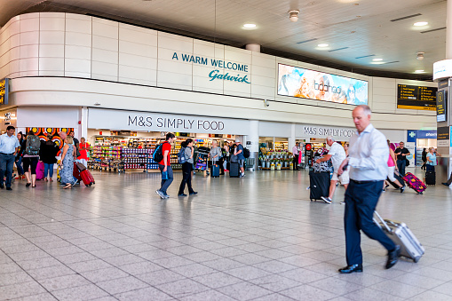 Horley, UK - June 28, 2018: Gatwick London airport terminal with people walking inside building architecture and sign for M&S grocery store simply food and welcome