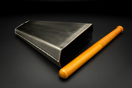 Closeup of a bongo bell with stick lying on a black background