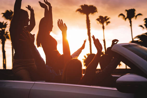 grupa przyjaciół bawiących się w kabriolet samochodowy podczas podróży o zachodzie słońca - młodzi podróżni jeżdżący kabrioletem podczas letnich wakacji - koncepcja szczęścia, wakacji i stylu życia młodzieży - outdoors car convertible wealth zdjęcia i obrazy z banku zdjęć