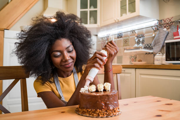 donne afro che decorano una torta a casa - home baking foto e immagini stock
