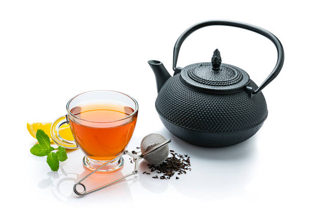 Black tea cup isolated on white background. A tea strainer, black teapot, lemon slices and a mint twig complete the composition.  High resolution 42Mp studio digital capture taken with Sony A7rii and Sony FE 90mm f2.8 macro G OSS lens