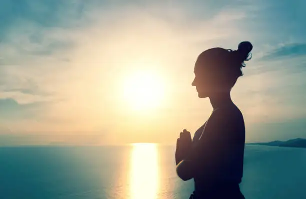 Photo of Woman meditating with namaste hands in the bright sunset light on the sea background, view from the side