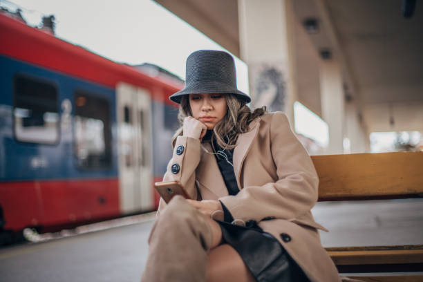 istock Young woman sitting on bench on the train station 1202979513