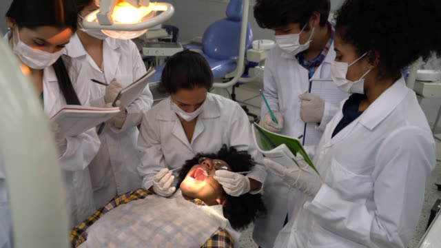 Female orthodontist examining a patient while students take notes and she asks questions