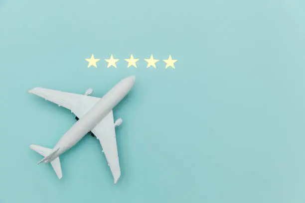 Photo of Simply flat lay design miniature toy model plane and 5 stars rating on blue pastel colorful trendy background. Travel by plane vacation summer weekend sea adventure trip journey ticket tour concept