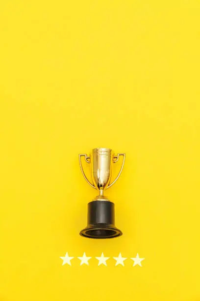 Photo of Simply flat lay design winner or champion gold trophy cup and 5 stars rating isolated on pink pastel background. Victory first place of competition. Winning or success concept. Top view copy space
