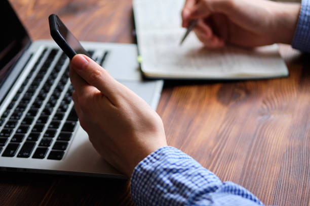 istock A man in a shirt rewrites information from a smartphone to a diary. Work concept. 1202982340