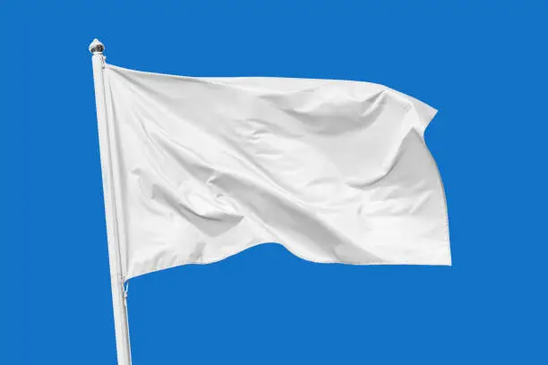 Photo of White flag waving in the wind on flagpole, isolated on blue background