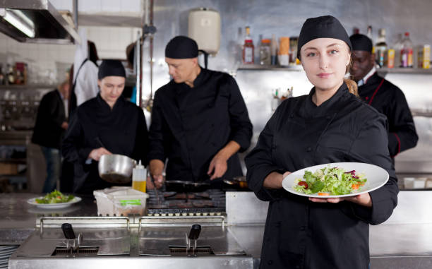 istock Positive female cook with cooked dish in restaurant kitchen 1203008052