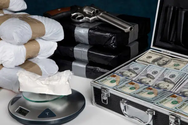 Confiscated illegal substance with measuring scale indicating 5 ounces, and a briefcase full of American currency.