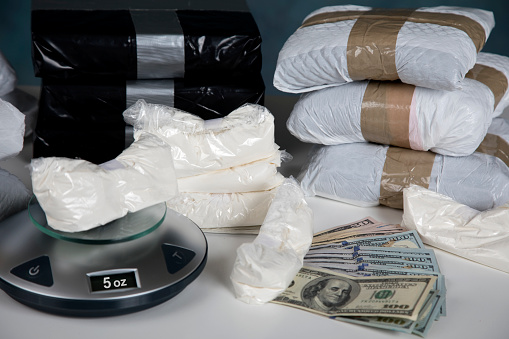 Confiscated illegal substance with measuring scale indicating 5 ounces, and a briefcase full of American currency.