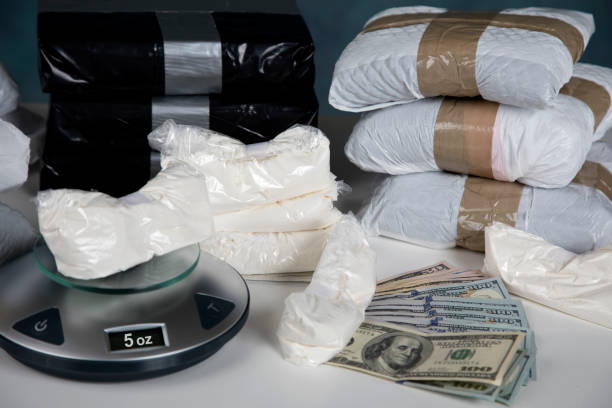 Illegal drugs on a scale with cash Confiscated illegal substance with measuring scale indicating 5 ounces, and a briefcase full of American currency. cocaine stock pictures, royalty-free photos & images