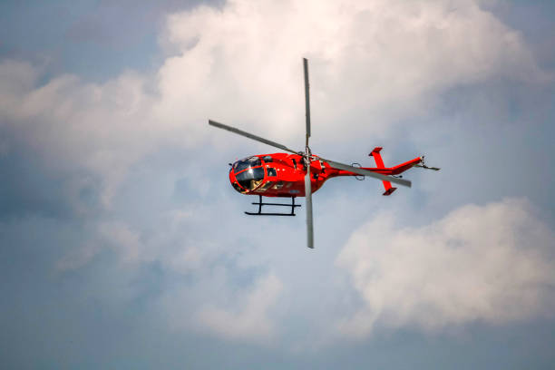 A red helicopter with propeller and blades is in the blue sky with clouds background