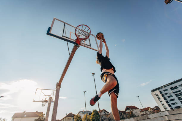 junger mann springt und macht einen fantastischen slam-dunk - streetball basketball sport men stock-fotos und bilder