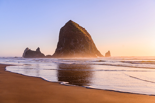 The sun sets behind the Haystack Rock formation on Cannon Beach in Oregon, USA.