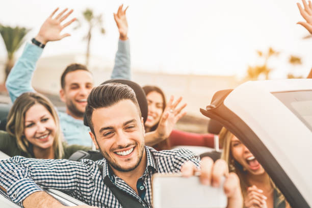 glückliche freunde machen foto-selfie mit handy-kamera im cabrio-auto - junge leute, die spaß im cabriolet auto während ihrer roadtrip-urlaub - reise und jugend-lifestyle-konzept - outdoors car convertible wealth stock-fotos und bilder