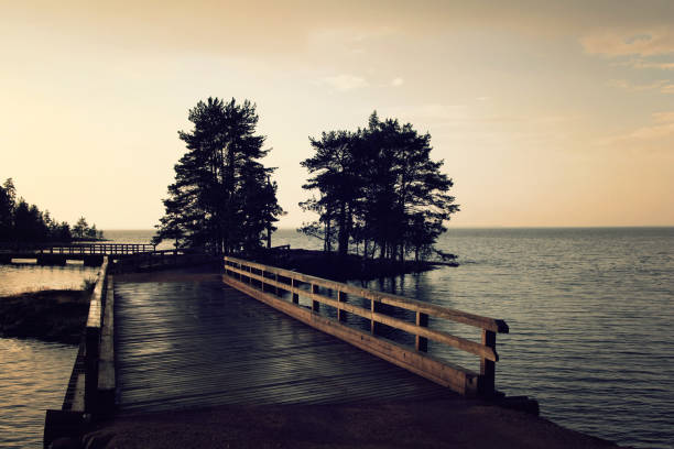 Pedestrian timber bridge on the Valaam island. Cloudy summer evening. Sunset. Rainy day. Russian north. Across the water. Valaam island, Karelia, Russia.