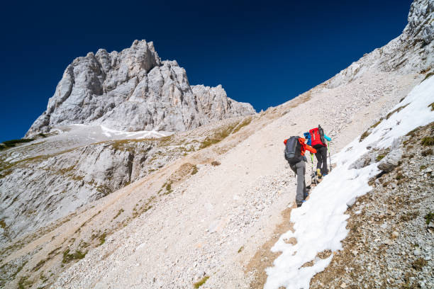 rear view mountaineer couple on difficult steep ascent through boulder and snow high up in alpine mountains in europe austria dachstein on sunny day in autumn with clear blue sky