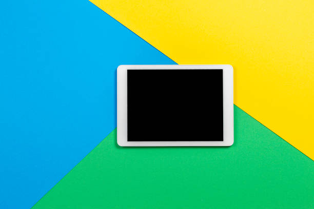 istock Digital tablet computer on light blue, green and yellow background. Top view 1203024048