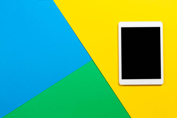 istock Digital tablet computer on light blue, green and yellow background. Top view 1203024123