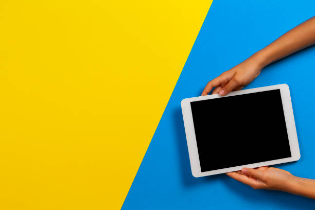 istock Kid hand with tablet computer on yellow and light blue background 1203024213