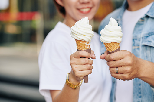 Unrecognizable couple on date holding tasty ice cream cones in their hands, horizontal close up shot