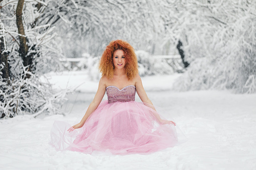 Winter fairy tale, a beautiful young girl in a luxurious lush pink dress enjoying the snowy forest