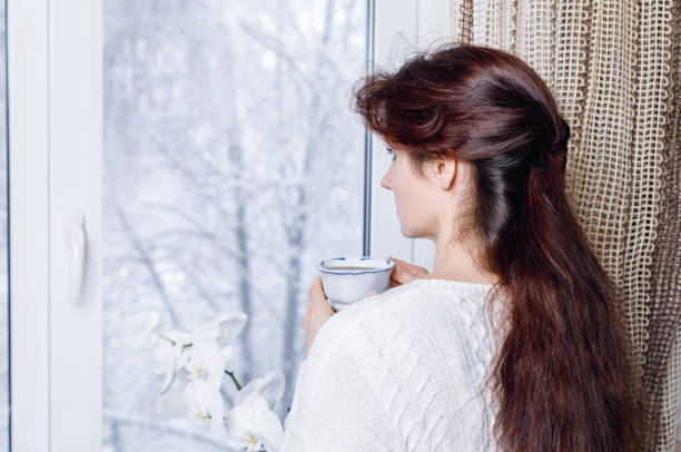 mujer con copa mirando por la ventana con naturaleza cubierta de nieve. - broken window glass women fotografías e imágenes de stock