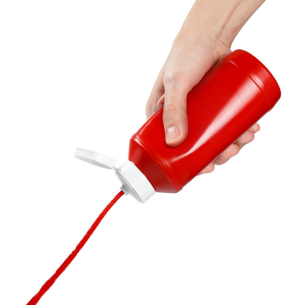 Hand squeezing ketchup out of a plastic bottle on white