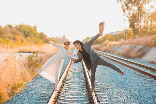 Asian Bride and groom feeling happy smiling and laughing while walk on railway, Wedding Couple at sunset with nature and copy space on background