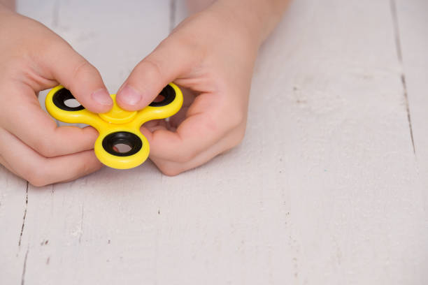 istock Child's hand spinning a fidget spinner device. Top view. Playing with a yellow hand spinner fidget toy 1203041437