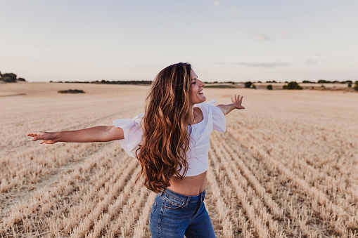 Summer Girl enjoying nature on yellow field. Beautiful young woman dancing Outdoors. Long hair in the wind. Happiness and lifestyle. Back view